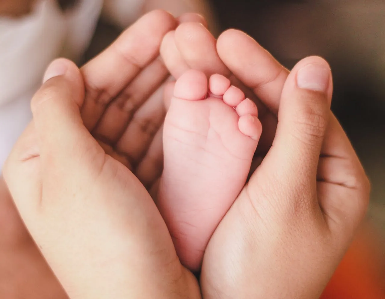 Newborn baby's foot cradled in caring hands — compassionate maternity and women's health care at Manikarnika Hospitals